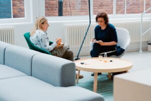 two woman sits on sofa chairs inside house