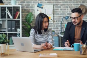 a man and a woman sitting at a table looking at a laptop